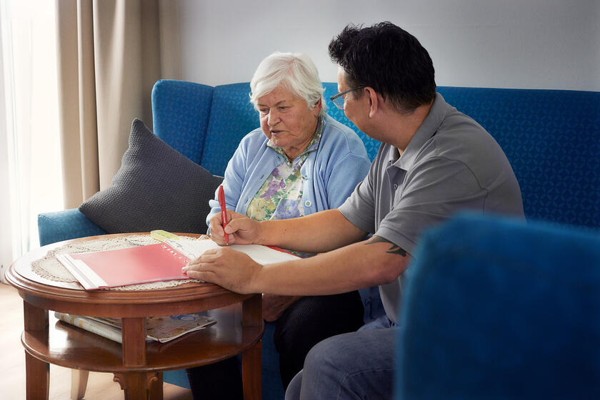 Ein Mitarbeiter der Johanniter bespricht mit einer älteren Frau Dokumente.