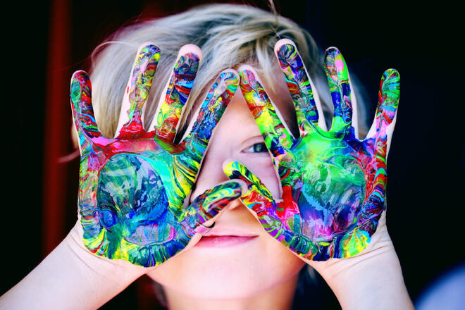 Ein Kind hält sich seine farbigen Handflächen vor das Gesicht.