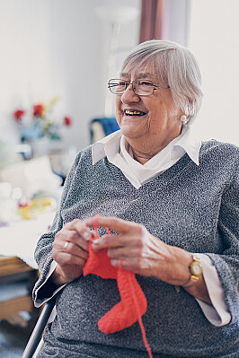 Eine Seniorin in grauem Pullover strickt