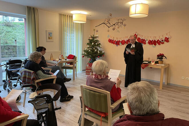 Ein Pastor singt mit Gästen vor einem Weihnachtsbaum