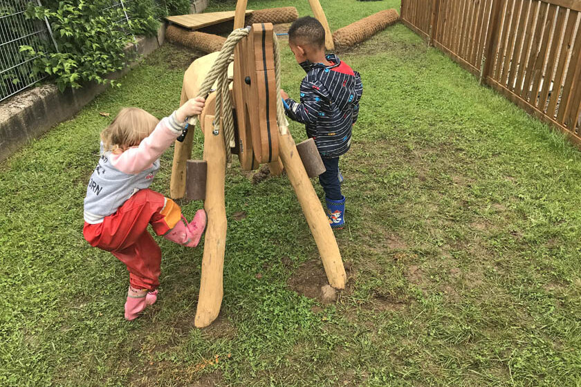 Zwei Kita-Kinder spielen im Außengelände mit dem neuen Holzpferd. 