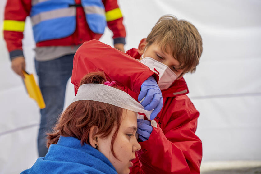 Ein Junge verbindet einer Patientin den Kopf bei der Teilnahme an einem Erste-Hilfe-Wettkampf. Im Hintergrund steht ein Schiedsrichter.
