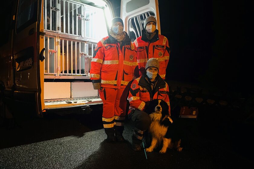 Drei Einsatzkräfte und ein Hund vor einem Einsatzwagen