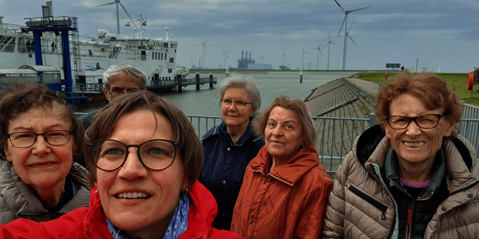 Fünf Frauen und ein Mann bblicken in die Kamera. Im Hintergrund sind Hafenanlagen und Windräder zusehen.