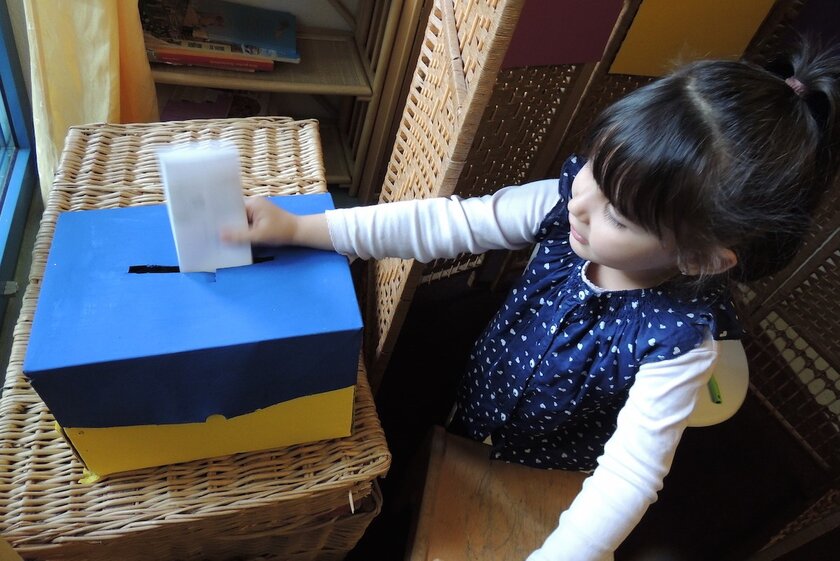 Ein Mädchen steckt einen Stimmzettel in eine Papp-Box.