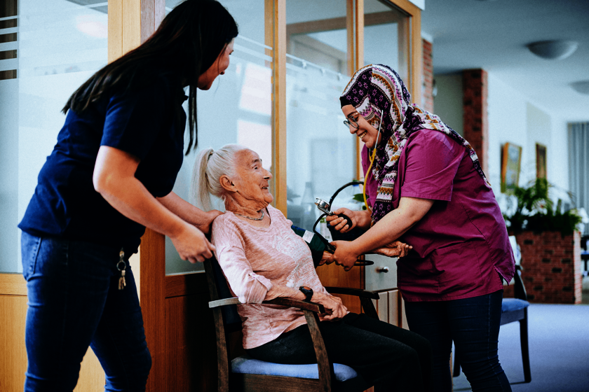 Zwei Pflegekräfte kümmern sich um eine ältere Dame, der der Blutdruck gemessen wird