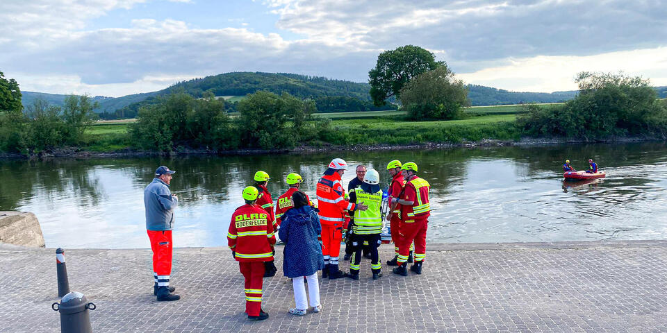 Einsatzkräfte von den Johannitern, der Feuerwehr und der DLRG am Ufer der Weser. Ein Rettungsboot ist zu sehen