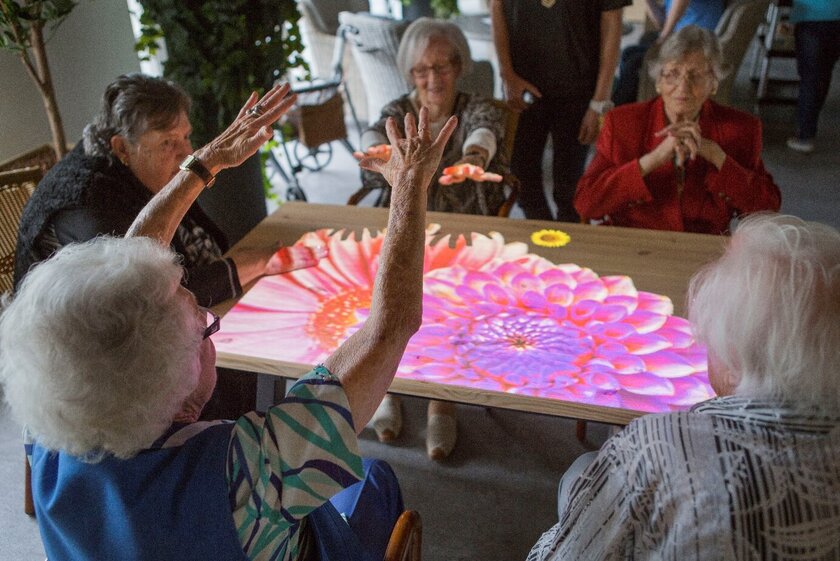 Gruppe von Senioreren spielen mit einer Blumen-Projektion über die  Tovertafel 