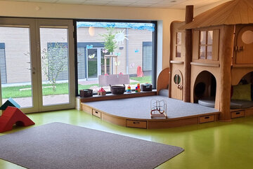 Lichtdurchfluteter Raum mit Spielteppichen und einen großen Holz-Spielhaus.