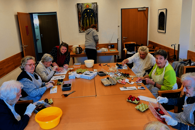 Gruppe von Menschen sitzt mit Malutensilien um einen Tisch