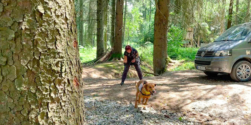 Eine Hundeführerin zeigt ihrem Hund im Wald die Richtung