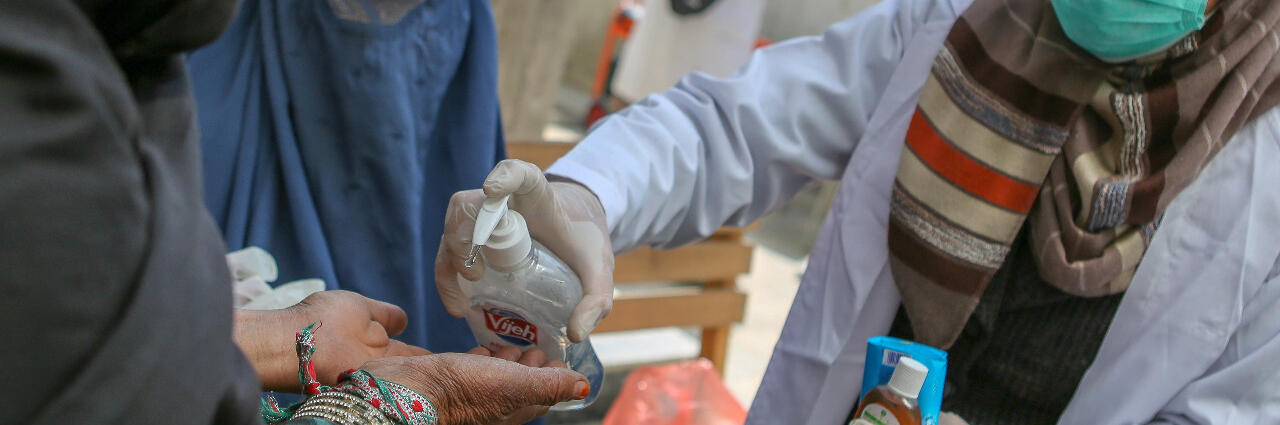 Eine Helferin verteilt Desinfektionsmittel an eine Frau.
