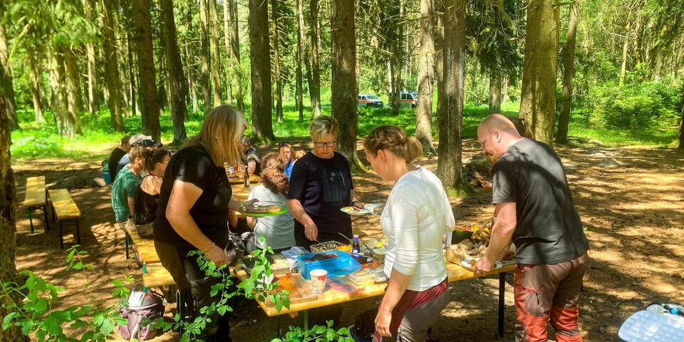 Personen bedienen sich an einem Tisch mit Essen im Wald