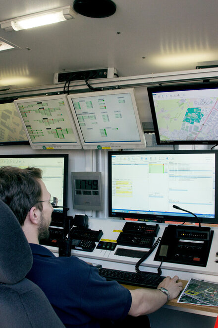 Zwei Führungskräfte des Katastrophenschutz vor Computer, Funkgerät und Monitor im Einsatzleitwagen