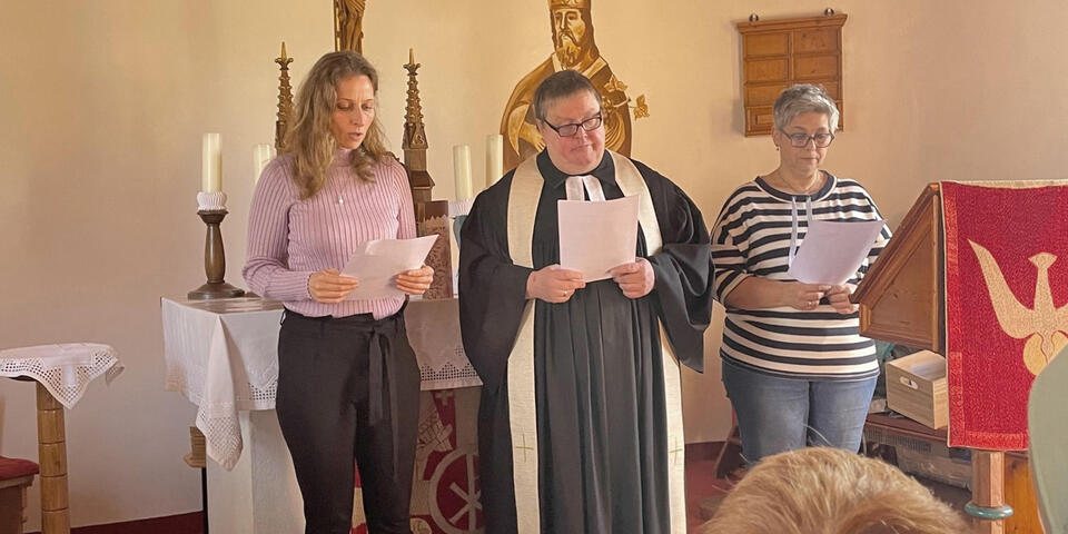 Kinder singen in einer Kirche gemeinsam mit einem Pfarrer und zwei Frauen