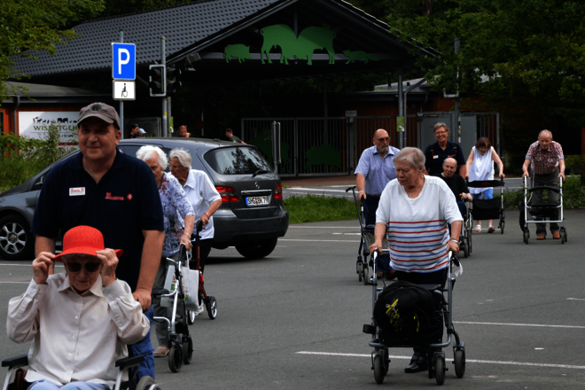 Senioren und Seniorinnen überqueren mit Rollatoren einen parkplatz. 