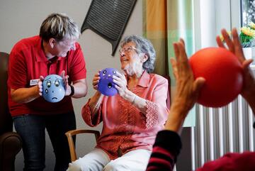 eine Pflegerin macht mit Senioren Übungen mit kleinen Bällen im Sitzen