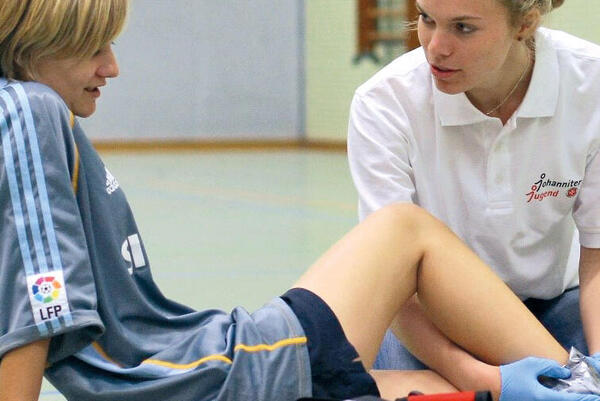 Schulsanitäterin kümmert sich um eine Schülerin nach einem Sportunfall