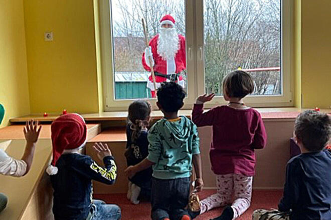 Kinder sehen durch ein Fenster den Weihnachtsmann kommen