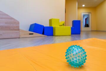 Ein Igelball liegt auf einer Matte. Im Hintergrund sind bunte, große Bausteine und eine Rampe zum Spielen zu sehen.