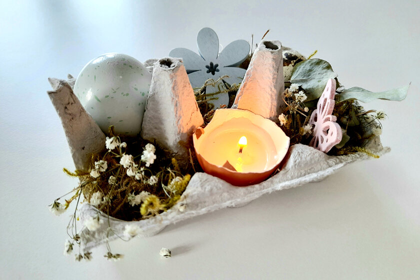 Ein Eierkaton dekoriert mit Blumen, Eiern und einer selbstgebastelten Kerze in einer Eierschale.