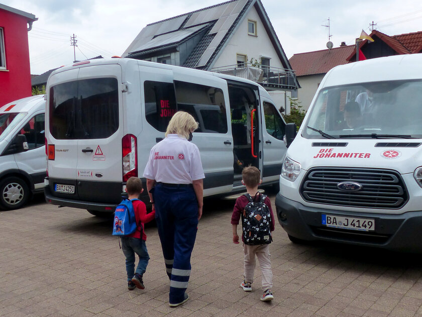 Eine Mitarbeiterin des Johanniter-Linienfahrdienstes begleitet zwei Kinder zum Bus.