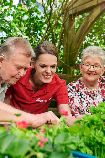 Eine Pflegerin der Johanniter ist mit zwei älteren Pflegepersonen im Garten.