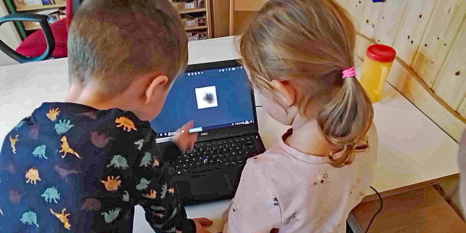 Kinder beobachten über einem Laptop die Aufnahmen einer Kamera in einem Abflussrohr