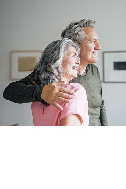 Älteres Paar steht lächelnd Arm in Arm.