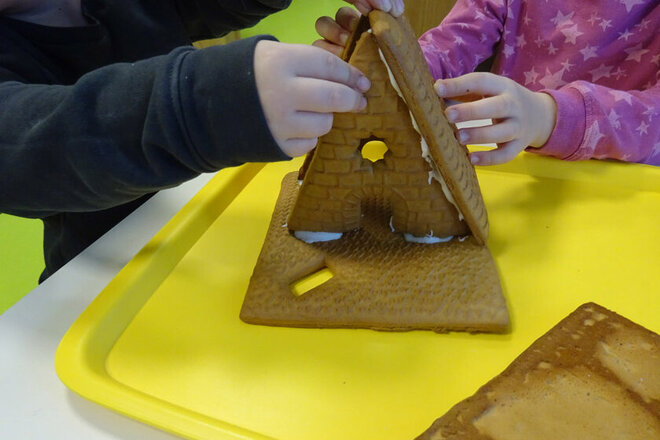 Zwei Kinder bauen ein Lebkuchenhaus auf.