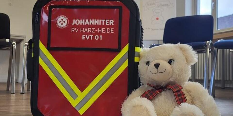 Teddybär sitzt vor einem Notfallrucksatz.