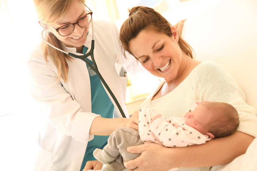 Ärztin bei der Untersuchung eines Neugeborenen in den Armen der Mutter