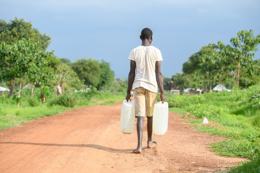 Lomuju geht mit einem Wasserkanister eine Straße entlang.