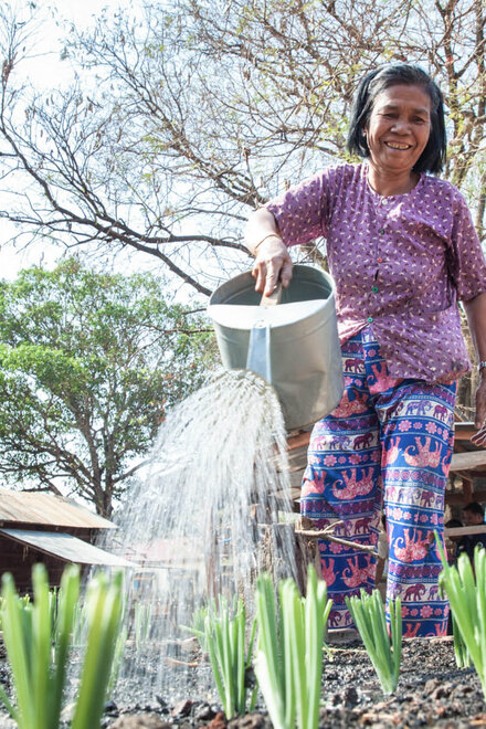 Eine Frau bewässert Pflanzen mit einer Gießkanne in einem Entwicklungsland.