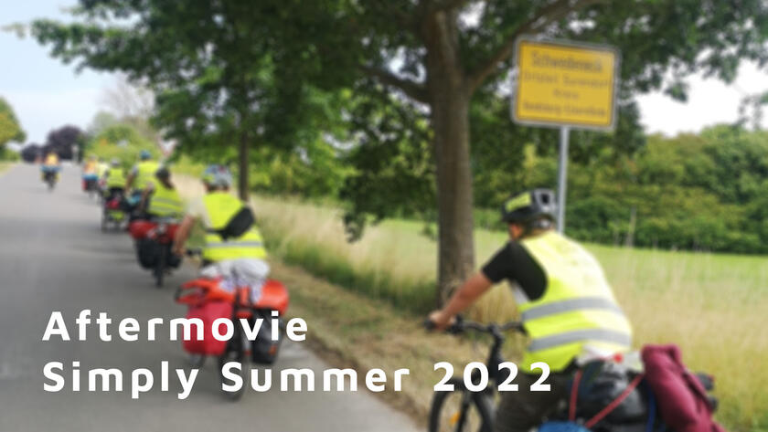 Mehrere Kinder fahren auf Fahrrädern entlang einer Straße. Das Bild ist unschard. Im Vordergrund steht der Text "Aftermovie Simply Summer 2022"