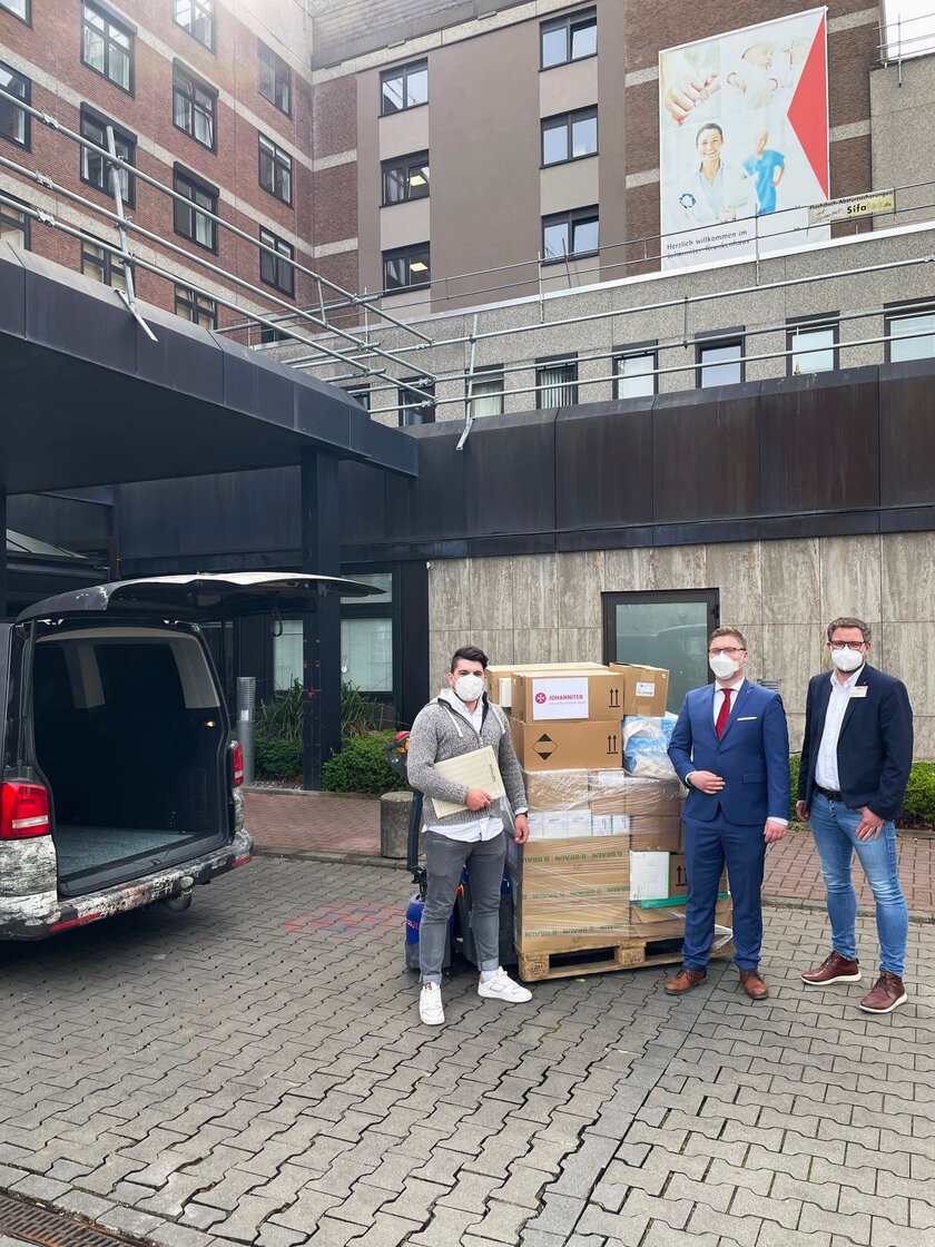 3 Männer mit Versandmaterial und Hilfsgütern für die Ukraine vor dem Eingang des Johanniter-Krankenhauses Bonn