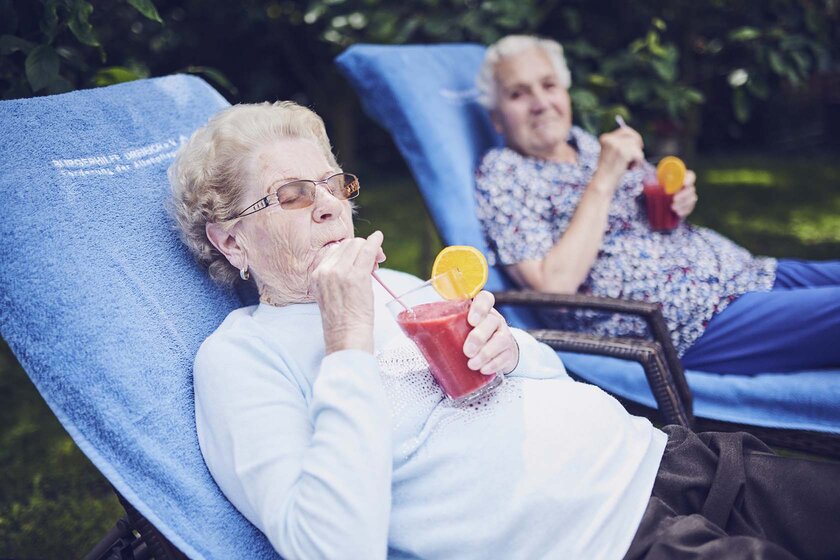 Zwei Bewohnerinnen im Liegestuhl genießen ein Kaltgetränk
