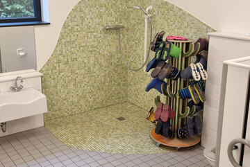 Sanitärraum mit kleinen Waschbecken und einer Vorrichtung zum Trocknen und Aufbewahren von Gummistiefeln.