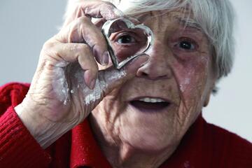 eine Seniorin schaut durch eine herzförmige Backform
