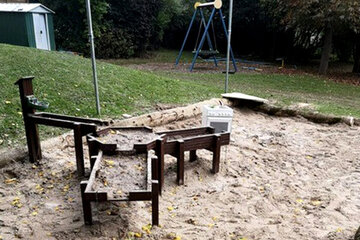 Sandkasten mit einer Holzspielanlage, durch die die Kinder Wasser fließen lassen können. 