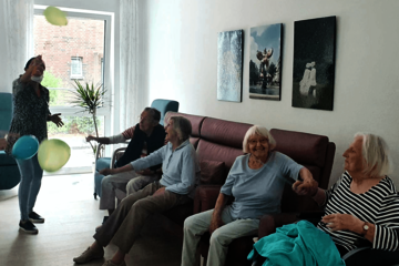 Vier ältere Menschen sitzen auf einem Sofa und beschäftigen sich lachend mit Luftballons.