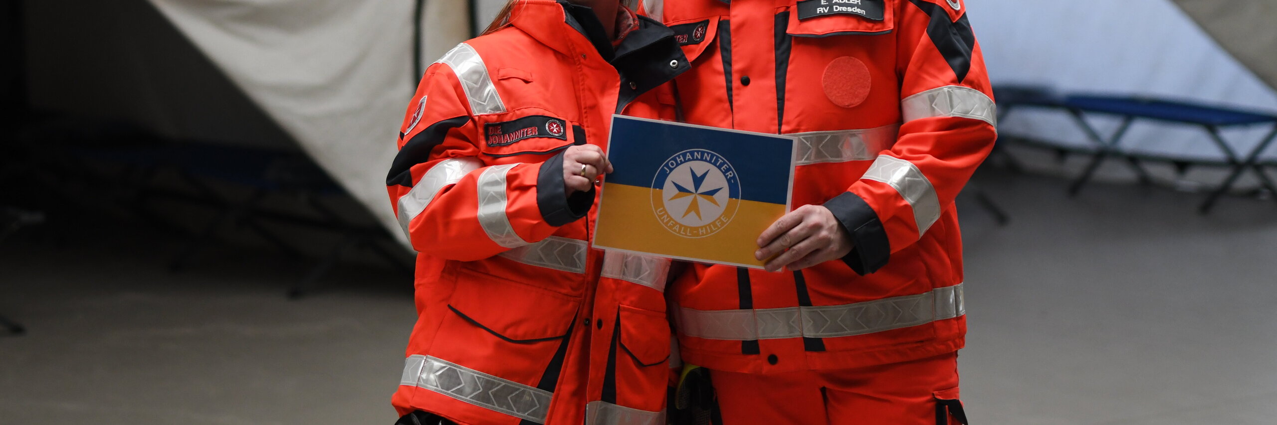 Zwei Johanniter halten ein Schild mit der ukrainischen Flagge