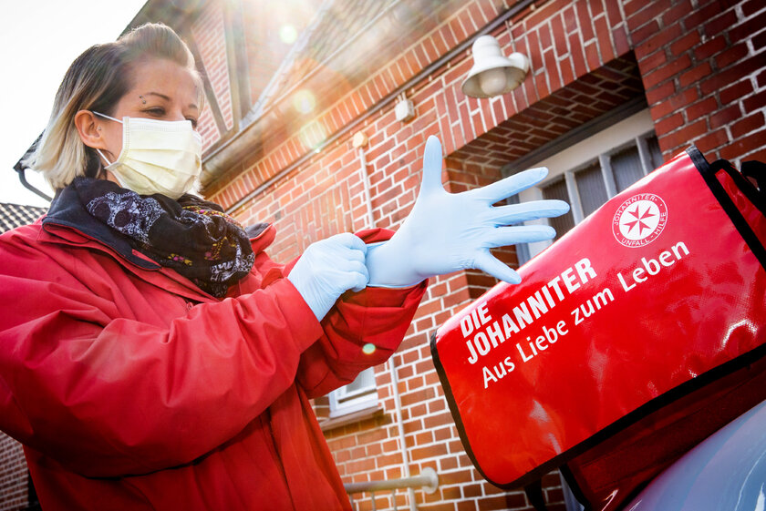 Eine Mitarbeiterin der Johanniter-Unfall-Hilfe legt sich Handschuhe und eine Atemmaske zum Schutz vor einer Corona-Infektion an.