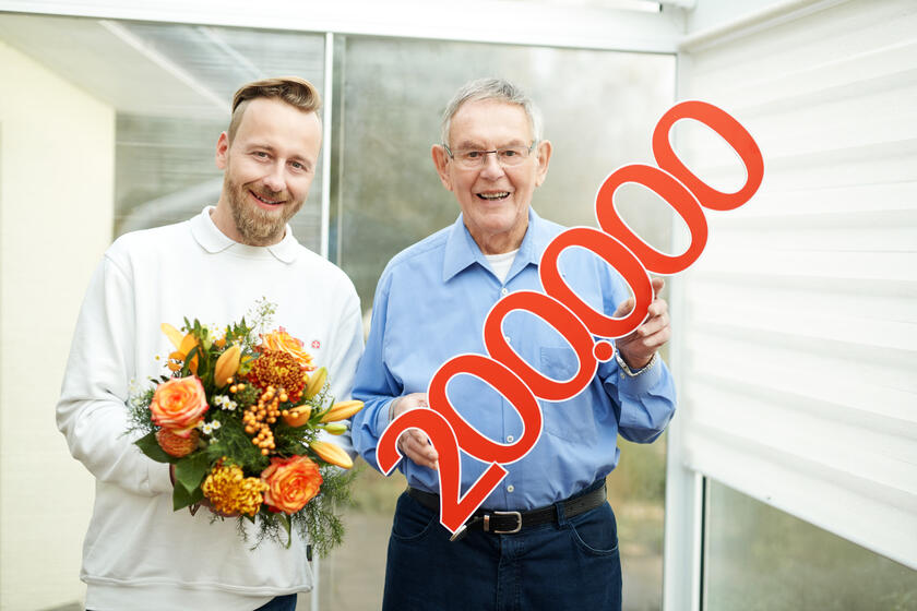 Ein Johanniter-Mitarbeiter überreicht einen Blumenstrauß dem 200.000sten Kunden