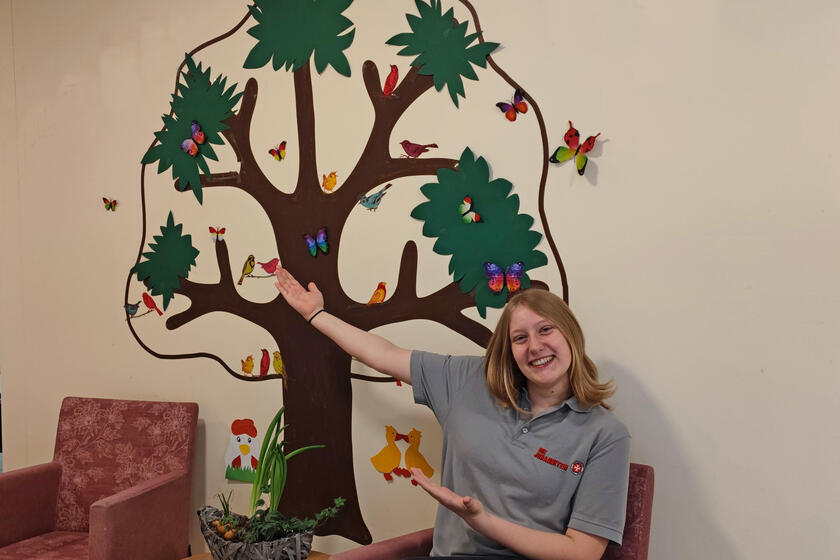 Eine junge Frau vor dem an die Wand gemalten Logo der WG - einem Baum