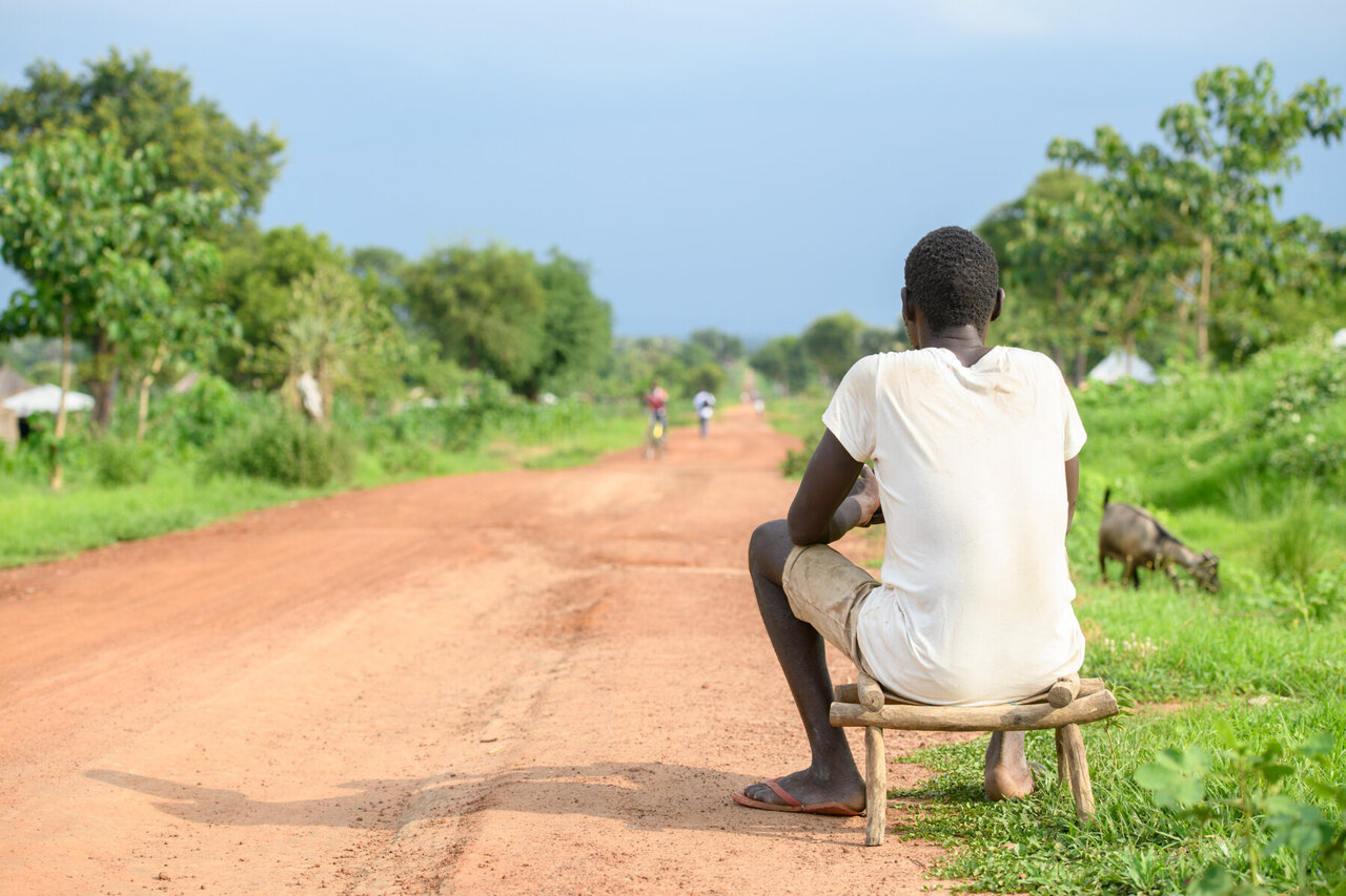 Lomuju is sitting on a chair, looking on the long road in front of him.