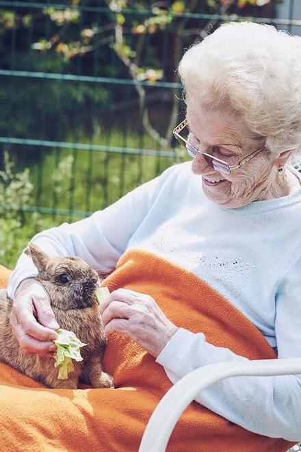 Eine Bewohnerin sitzt im Garten und streichelt Kaninchen