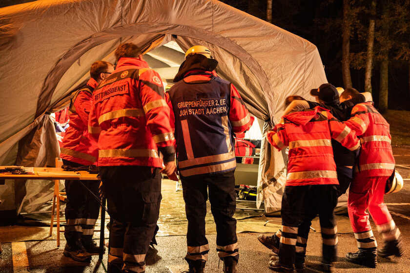 Katatrophenschützer in Einsatzkleidung bringen verletzte Personen in ein großes Zelt
