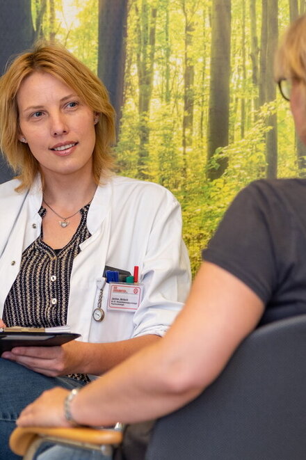 Ärztin bei einem Gespräch mit einer Patienten vor einer Waldtapete