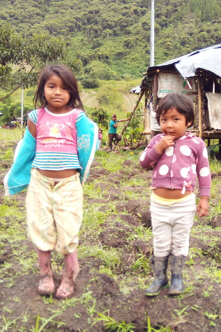 Zwei kleine Mädchen stehen in schmutziger Kleidung auf einem Feld. Im Hintergrund ist eine Holzhütte